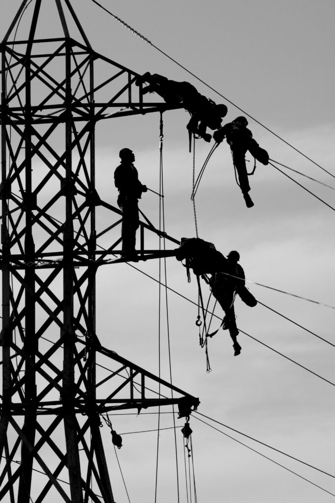 Vier Männer auf einem Strommast. Sie scheinen eine Installation von Kabeln durchzuführen.